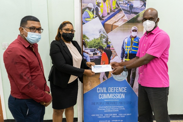 (Left to right) Laparkan’s Coordinator Mr. Ulric Paul looks on as Operations Manager, Ms. Sherry Singh presents a cheque to Civil Defence Commission, Director General, Lieutenant Colonel, Kester Craig.